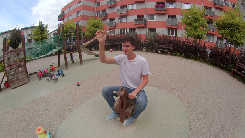 Happy adult guy posing in the playground. A rider with a toy spear on a wooden horse. Outdoor lifestyle.