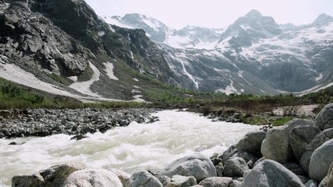 Scenic landscape with a fast mountain river flowing between rocky stones. The waterfall falling from top of mount. Snow and glaciers on mountain slopes. Caucasus mountains. North Ossetia - Alania