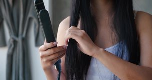 Close-up of unrecognizable woman with beautiful bright healthy long hair using flat iron straightener for straightening hair at home bathroom. Hair care, hairstyle, fashion concept. Beauty routine