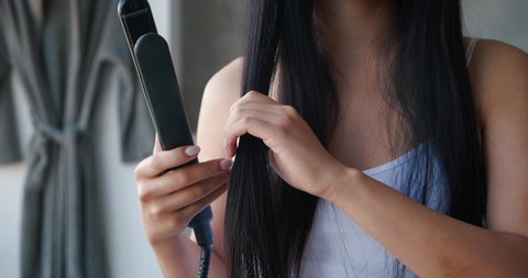 Close-up of unrecognizable woman with beautiful bright healthy long hair using flat iron straightener for straightening hair at home bathroom. Hair care, hairstyle, fashion concept. Beauty routine