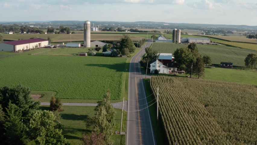 Aerial reveal above road through rural American countryside. Homes and farms along country road. Royalty-Free Stock Footage #1081703684