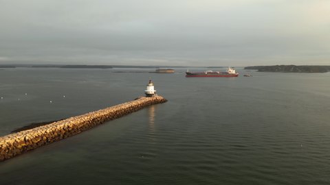 The Spring Point Ledge Lighthouse off the coast of Maine with large shipping vessel in background