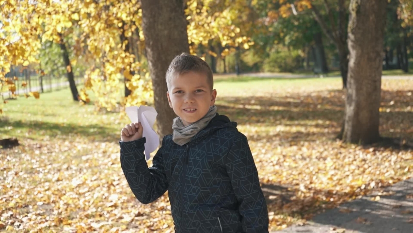 A Boy in the Autumn Colorfull Park Play With a Paper Plane. The Concept of a Happy Child. Happy Family Childhood a Slow Motion Lifestyle Video Concept. Child Launch the Paper Plane