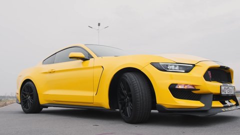 Yellow Ford Mustang with black stripes stands in a parking lot. Fly the camera around the car. Russia, Rostov-on-Don 23 Oct2021

