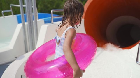 Cute little girl jump and start from the water slide in aqua park. happy kid funny start rolling down the slide. Entrance to the slide of the water park
