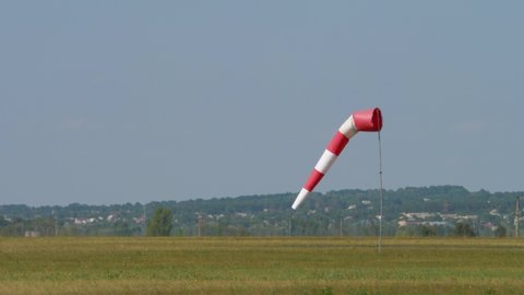 Red white cone airsock swings in wind on sky background. Indicator of wind direction and speed. Visual signal at airport. Small plane landed on runway