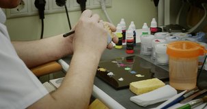 Dentist dental technician selects the color and applies paint to the denture (model jaw) with a brush in the dental laboratory.
High quality 4k video. Shot with RED camera.