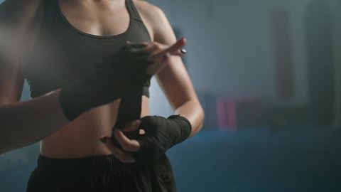 Woman fighter wraps her hands with boxing bandages, kickboxing training day in a gym, female fighter is preparing for battle, 4k slow motion.