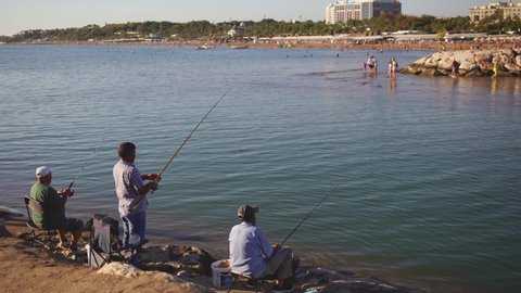 Evrenseki, Side, Turkey - October 24, 2021: Many people fishing happily on sea shore using fishing rods during sunset time