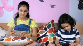 Brother and sister using a tablet and smartphone at home - Technology burden for kids. An elder sister and her adorable brother are busy playing games on their mobile during the lockdown period