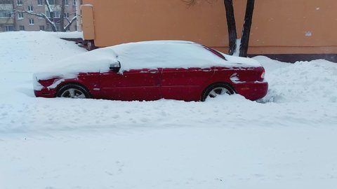 A parked passenger car under a layer of snow in the yard. Snow storm in winter