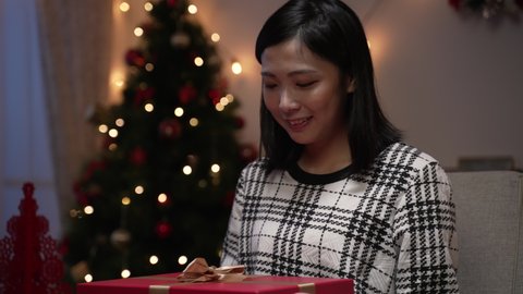 asian female unboxing her Christmas gift is feeling frustrated about getting unwanted item and smiling to lie about pleasure while saying thanks