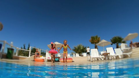 Two little girls jumping in swimming pool at summer sunny day. Happy children have fun on vacation at tropical resort. Slow motion, childhood, family concept