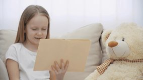 4k slowmotion video of little girl reading a book to her teddy bear.