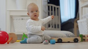 Baby sitting on the floor playing with toys from toy storage basket, cute 7 month old baby boy having fun exploring new world around him at home. High quality 4k footage