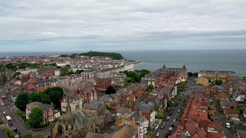 Aerial drone footage of the town centre of Scarborough in the UK, showing the residential housing estates and historical town houses by the seaside going along to the beach front on a cloudy day