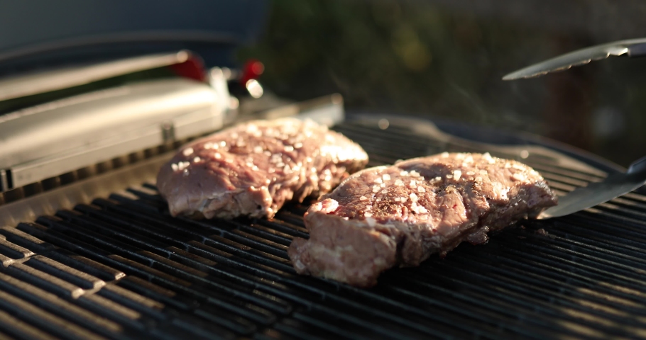 Man roasted meat on the gas grill on barbecue grill outdoor in the backyard, grilled steak meat, summer family picnic, food on the nature. Royalty-Free Stock Footage #1081734878