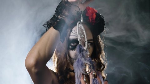 Lady model with wreath on head choker and in lacy cuffs poses with dreamcatcher in hands in smoke cloud at artificial studio light closeup