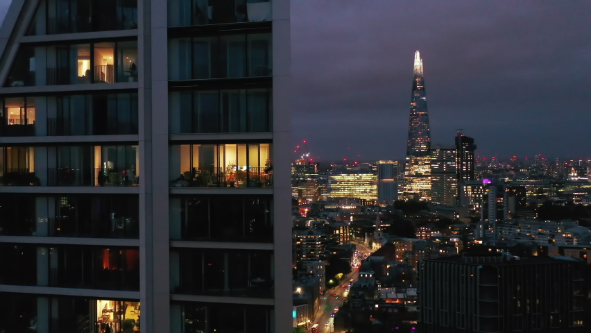 Elevated forwards fly around modern tall apartment building. Revealing panoramic view of night cityscape. London, UK