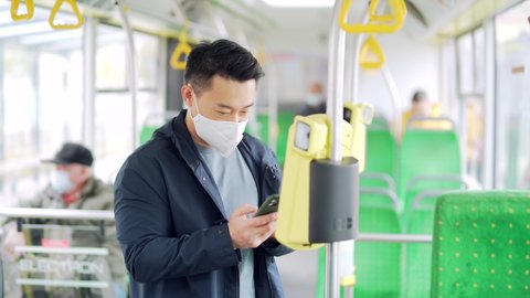 Asian man paying public city transport with mobile phone app. male passinger in a face mask bought validating bus ticket using conctactless smartphone. ride inside trolleybus or tram use application