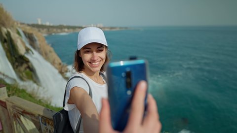 attractive smiling woman tourist making selfie on mobile phone on Lower Duden Waterfall background in Antalya. Famous view point on mediterranean sea coast in Turkey.