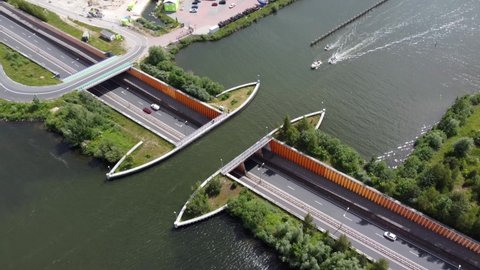 Aerial drone view of aqueduct or water bridge constructed to convey watercourses across gaps showing recreational boats moving towards the infrastructure and traffic going underneath it 4k quality