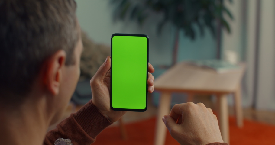 View from shoulder of caucasian man doing swipe up gesture on chroma key of modern smartphone. Mature male resting at home and using cell phone. Royalty-Free Stock Footage #1081742384