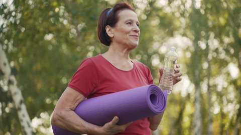 Elderly woman with yoga mat drinks water