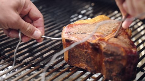Professional barbecue man checking meat steak readiness putting thin thermometer inside the meat, premium meat steak roasting on bbq grid for picnic party. Process of grilling meat steaks for luxury