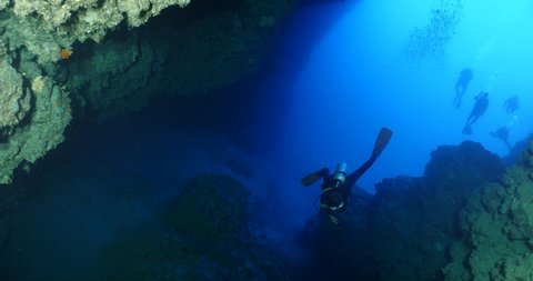 scuba divers exploring around a reef underwater deep blue water big rocks and bubbles ocean scenery