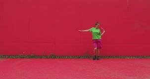 Dancing young happy girl perform energetic expressive dance against red wall. Modern joyful female dancer cool moving