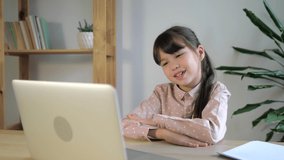 Little caucasian girl making online video call waving Hello to laptop computer webcam. Kid sitting at home and studying. Online school, e-learning concept, homeschooling. Children remote education.
