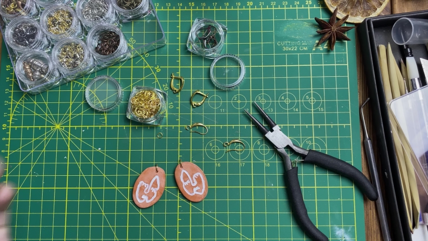 Women's hands make earrings. Master connects clay face figures and ear wires with metallic rings. Tools for handmade jewelry. Leisure and craft. | Shutterstock HD Video #1081757699