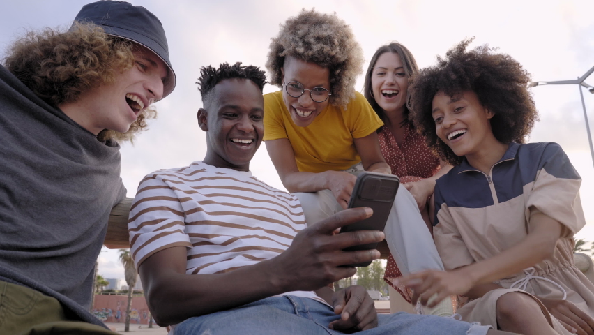 Happy smiling teenage friends laughing outside at something in smartphone or mobile phone. Young multiracial people spending time together. Friendship, communication, youth and lifestyle concept | Shutterstock HD Video #1081758380