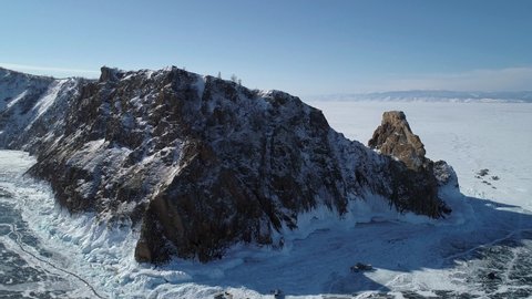 Aerial view of the cape Khoboy, Olkhon island. Tall rocks in frozen lake Baikal with many people and cars around. Popular touristic destination. Winter landscape. Panoramic view. Tilt shot