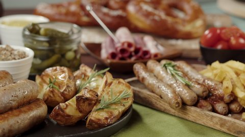 Traditional German Cuisine. Putting tray with smoked sasuages and fried potatoes, pickled cucumbers, bratwursts and fresh pretzels on table. Composition of Cooked National Czech Food. 