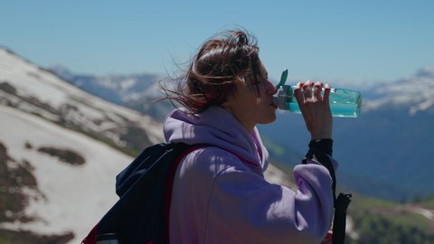 Slow motion shot of young woman backpacker is thirsty and drinking water after long hiking in the mountains. A sigh of relief when taking a gulp