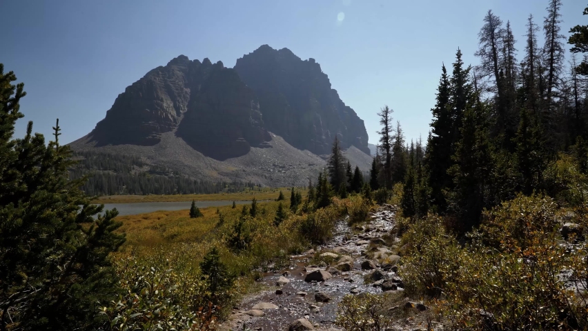 Stunning nature landscape view of the incredible Red Castle Peak up a backpacking trail in the High Uinta National Forest between Utah and Wyoming with a small babbling brook and pine trees.
