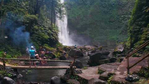 Bali, Sidan - Indonesia - Sep 4 2021: Travel people enjoy beautiful waterfall Nungnung on background tropical rainforest jungle in Bali, Indonesia 4K Aerial view