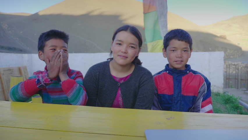 Shot of three young mixed-gender east Asian kids with smiles on their faces sitting outdoors together on a bench and looking at the camera in a mountainous cold region or terrain. Royalty-Free Stock Footage #1081767335