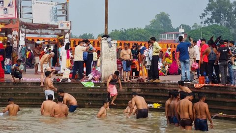 Haridwar, Uttarakhand, India - circa 2021 : panning shot of people bathing at har ki podi ghat riverbank of holy Ganga where people go to dip and wash away their sins and for religious purposes