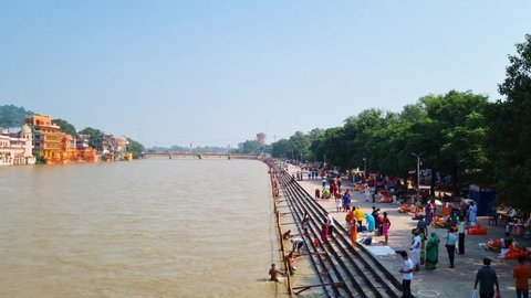 Haridwar, Uttarakhand, India - circa 2021 : wide shot showing the huge holy river ganga with the stairs on the ghat riverbank where devotees are taking a bath dipping as part of ceremonies  