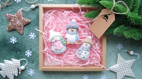 Hands putting Christmas toys, snowmen and penguin in knitted hats and scarves in a gift box. Cozy Christmas concept. New Year's decor, DIY gift wrapping. 4 k, slow motion.