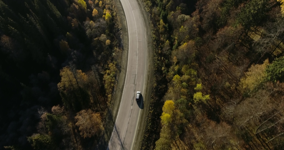 One gray silver crossover SUV car driving alone road trip, travel on freeway through dense colorful forest corridor at autumn sunny sunset - Aerial drone wide view