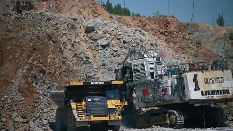 Russia, Amur region, July 7, 2021. Quarry, open pit mining, gold ore mining. The ore is loaded by a Liebherr excavator into a Caterpillar truck from the quarry. Summer.