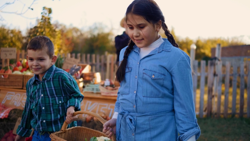 Brother and sister carry their own vegetables with a smile. Little boy and a girl help their grandfather in the village. Family business local market organic food