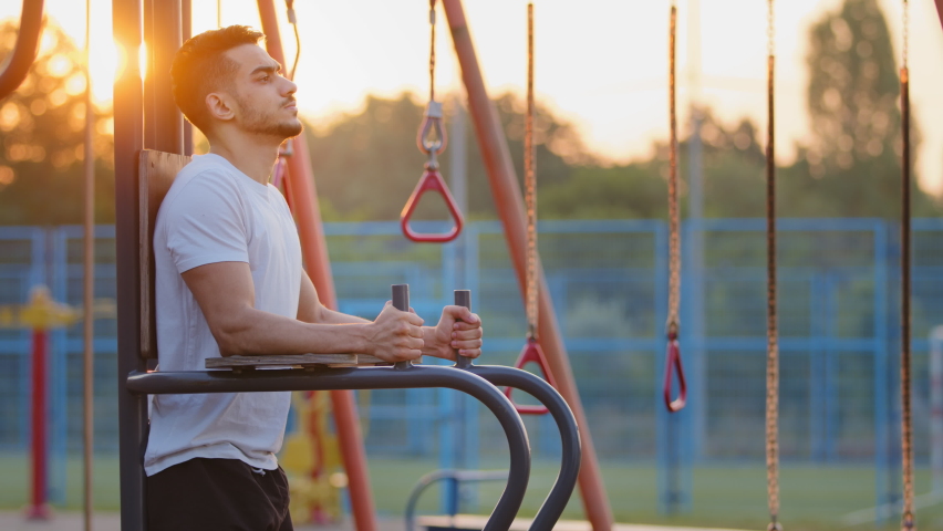 Adult handsome strong sporty Indian guy raises knees high, training abs during morning workout. Middle Eastern athletic young man exercising outdoor at sports ground, pumps up muscles using equipment Royalty-Free Stock Footage #1081781477