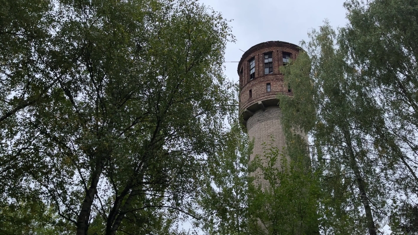 Old high water tower surrounded by trees. Brick tower in countryside.