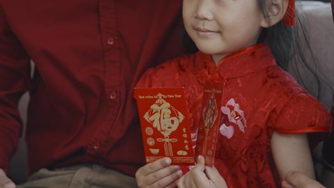 Mid-section shot of unrecognizable father touching cheek of cute Asian 5-year-old girl in traditional tang suit holding Chinese New Year postcards