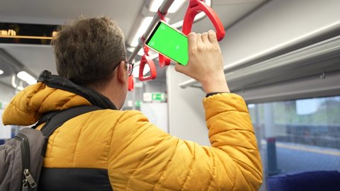 Tired plus size man rides suburban train holding smartphone with green screen, back view.